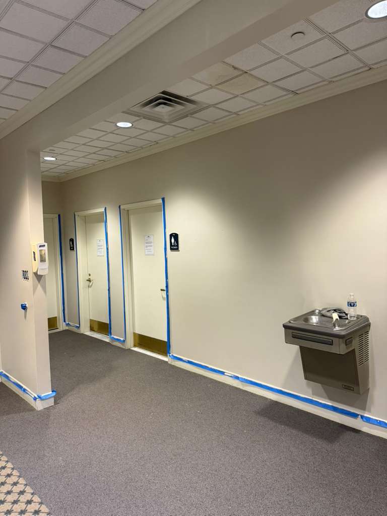 Hallway with white doors and a water fountain, taped off with blue painter's tape.