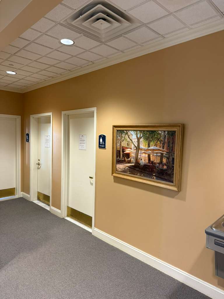 Tan hallway with white doors, a restroom sign, and a framed outdoor cafe painting.